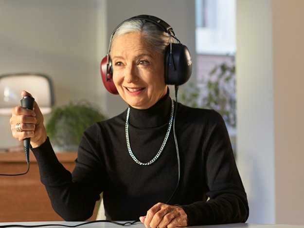  Kvinna med hörlurar som gör ett hörseltest och håller i en svarsknapp.