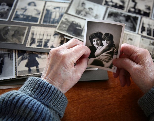  En äldre person med hörselnedsättning håller i ett gammalt fotografi och ser på ett fotoalbum, en påminnelse om kopplingen mellan minnet och obehandlad hörselnedsättning.