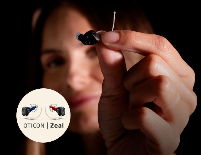 Kvinna som håller upp Oticon Zeal hörapparaten i en hand
