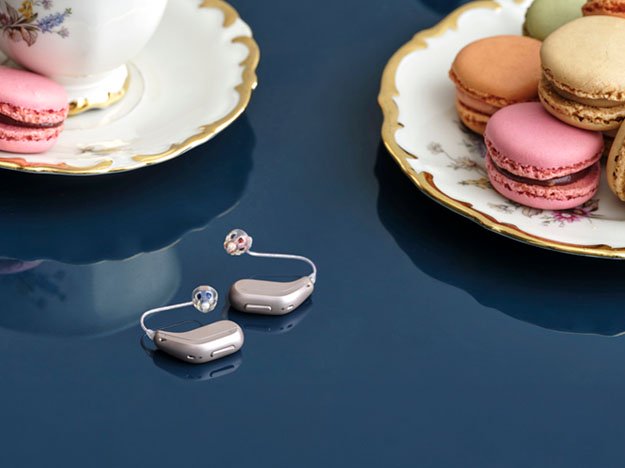 Hörapparater på ett bord bredvid tefat och makroner, hjälpmedel som kan lindra tinnitus.