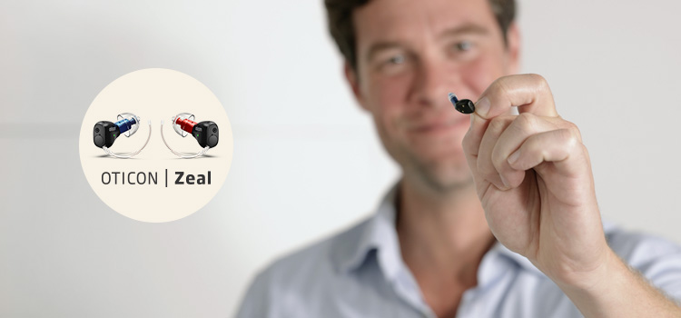 Man som håller upp hörapparaten Oticon Zeal som du kan prova ut på Audikas hörselklinik