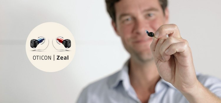 Man som håller upp hörapparaten Oticon Zeal som du kan prova ut på Audikas hörselklinik
