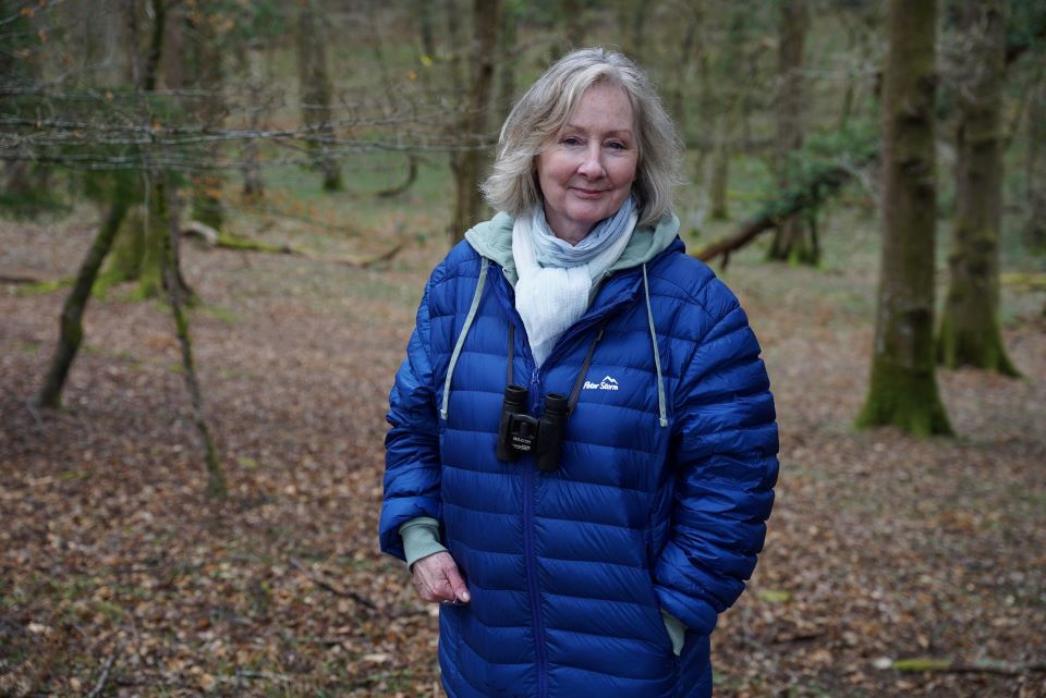 Woman birdwatching in a forest while wearing a blue jacket and binoculars.