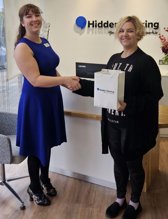 A woman at an Audika clinic receives a packaged set of hearing aids to assist with hearing loss and tinnitus.