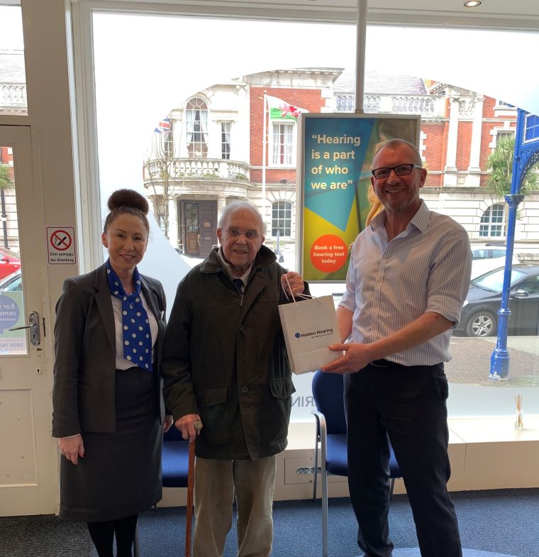 Hearing care clinic team presenting an Audika gift bag to an older man as part of a community give back programme.