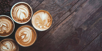 Five cups of latte with intricate foam art on a rustic wooden surface.