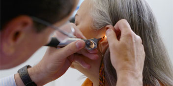 Hearing specialist performing an ear examination on an older woman
