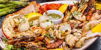 Seafood platter with grilled shrimp, scallops, lobster, and lemon wedges alongside asparagus and dipping sauce