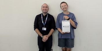 Audika Give Back Programme donation recipients standing against a plain wall, with one person holding a Audika branded bag.