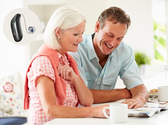 Bernafon Encanta hearing aid beside an older couple sitting at a table, discussing and reading together in a bright, homey setting.