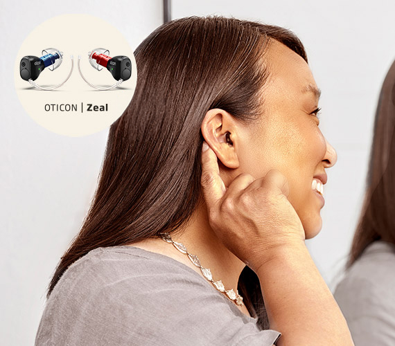 A person adjusts an in-ear hearing aid in a modern indoor setting. The image highlights ’Oticon Zeal’ hearing aids, showcasing discreet, high-performance hearing solutions.