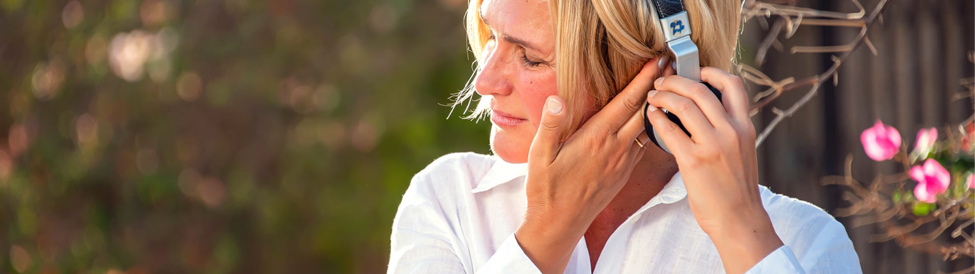 Woman adjusting headphones outdoors while touching her ear.