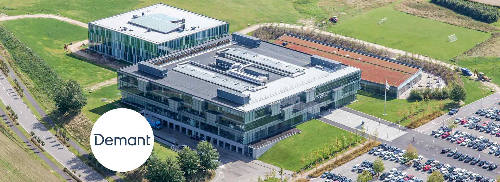 Demant headquarters building in Kongebakken, featuring sustainable architecture surrounded by green spaces and parking areas.