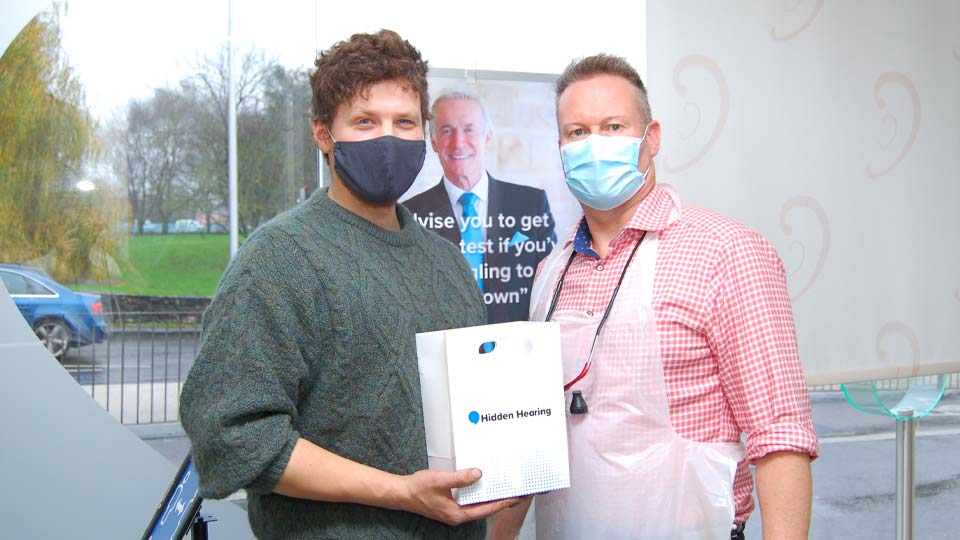 Audika customer Matthew Blackwell holding a Audika-branded bag alongside a staff member.