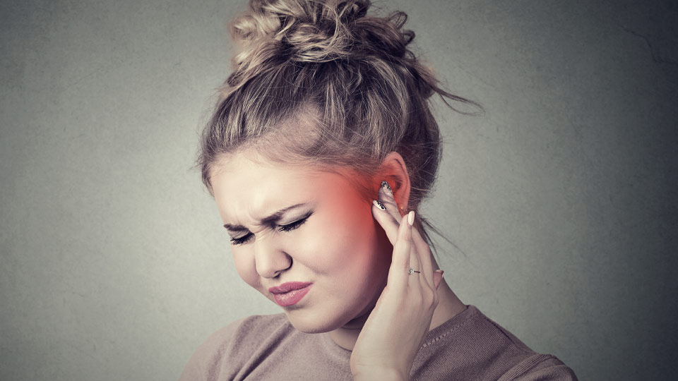 Girl experiencing ear pain while touching her ear, possibly due to an outer ear infection.
