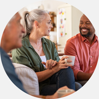 Woman with gray hair holding a coffee cup appears disengaged in a group conversation due to untreated hearing loss.