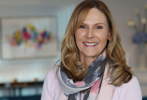 Audika ambassador Sandra Pierce wearing a patterned scarf in a softly lit room with abstract wall art in the background.