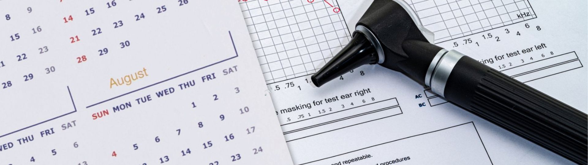 Otoscope placed on audiogram and hearing test paperwork next to a calendar