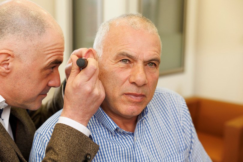 A clinician uses an otoscope to examine a patient's ear during a hearing test in a well-lit hearing clinic, featuring comfortable seating and a professional, discreet environment.