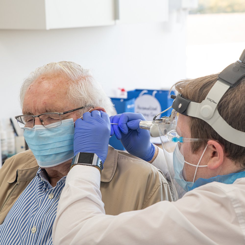 An audiologist uses specialized tools and a headlight to examine a senior patient's ear in a modern hearing clinic.