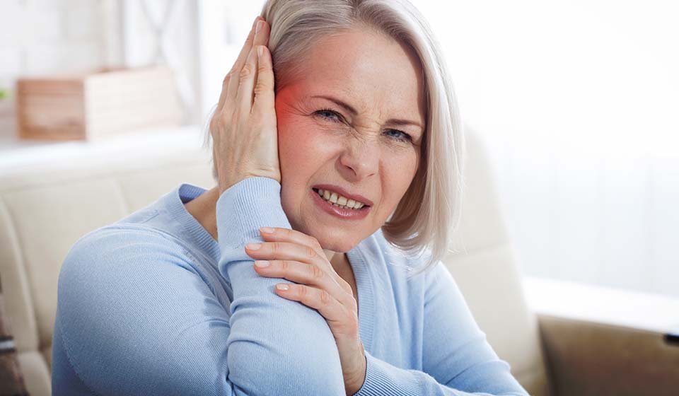 woman experiencing ear pain while sitting indoors