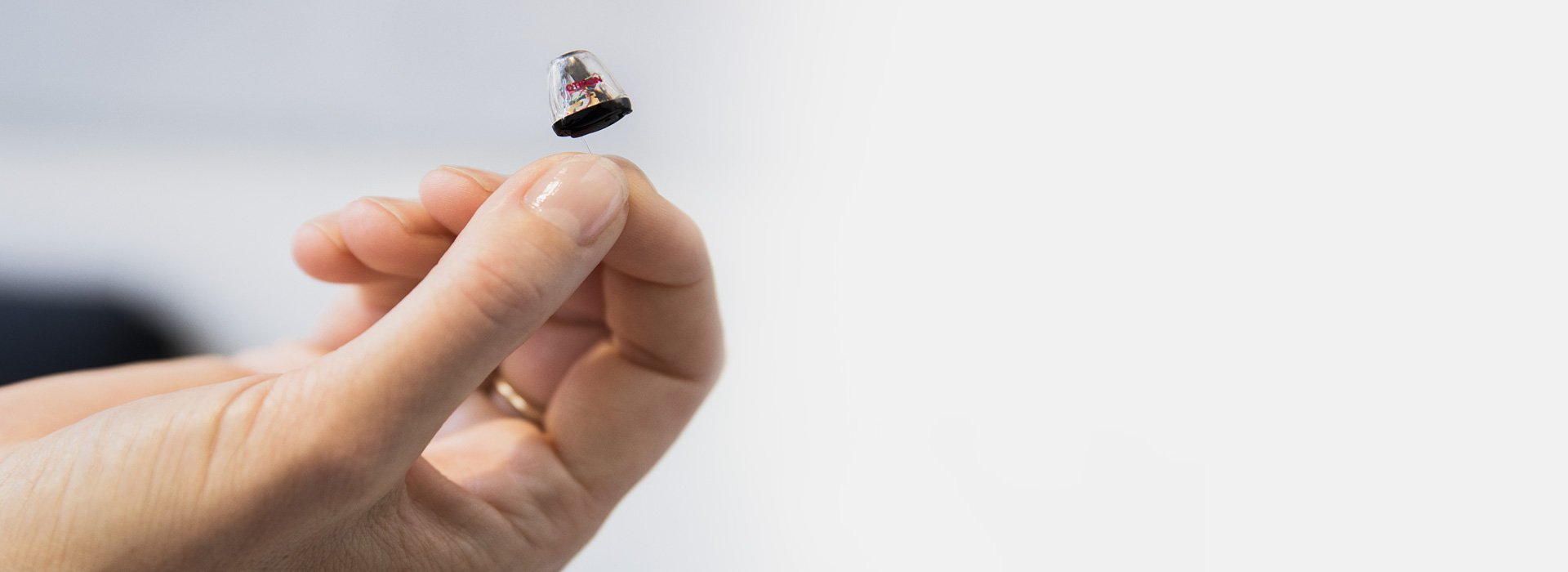 A hand delicately holds an invisible-in-the-canal (IIC) hearing aid in a bright, minimalistic setting. The advanced device highlights discreet hearing solutions offered by Hidden Hearing for personalized audiology care.