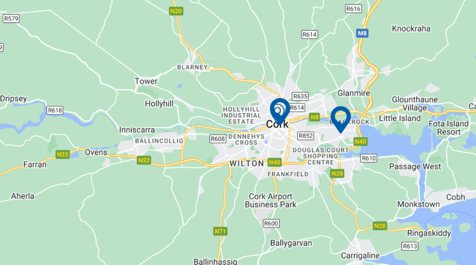 A map highlighting two locations in Cork, Ireland, marked by pins. One pin features a stylized ear icon, possibly representing a Hidden Hearing clinic or audiology center. Nearby roads include the N22 and M8 highways, with notable areas such as Ballincollig, Douglas Court Shopping Centre, and Fota Island Resort shown for context. No text is visible within the image.