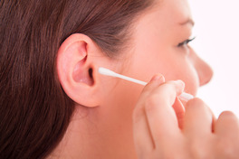 Close-up side view of a person inserting a cotton swab (Q-tip) into their ear while cleaning it.