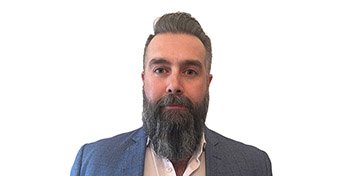 [GEN] A person with a blurred face stands against a plain white background, wearing a blue suit jacket over a light-colored shirt, featuring a prominent, well-groomed beard. No visible text or hearing aids are identifiable.