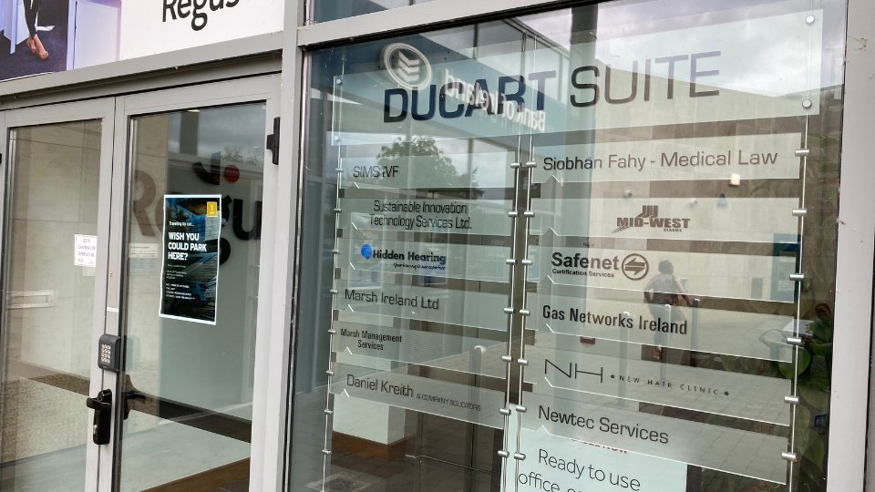 The glass-front entrance to 'Ducart Suite' displays branded signage, including 'Hidden Hearing' specializing in hearing care. Other listed businesses include medical law, technology, and certification services. A poster reads: 'Wish You Could Park Here?'