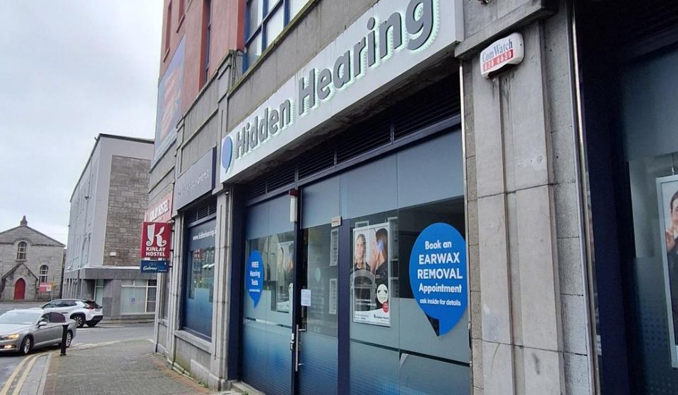 The storefront of 'Hidden Hearing,' a hearing clinic, displays signage promoting 'FREE Hearing Tests' and 'Book an EARWAX REMOVAL Appointment.'