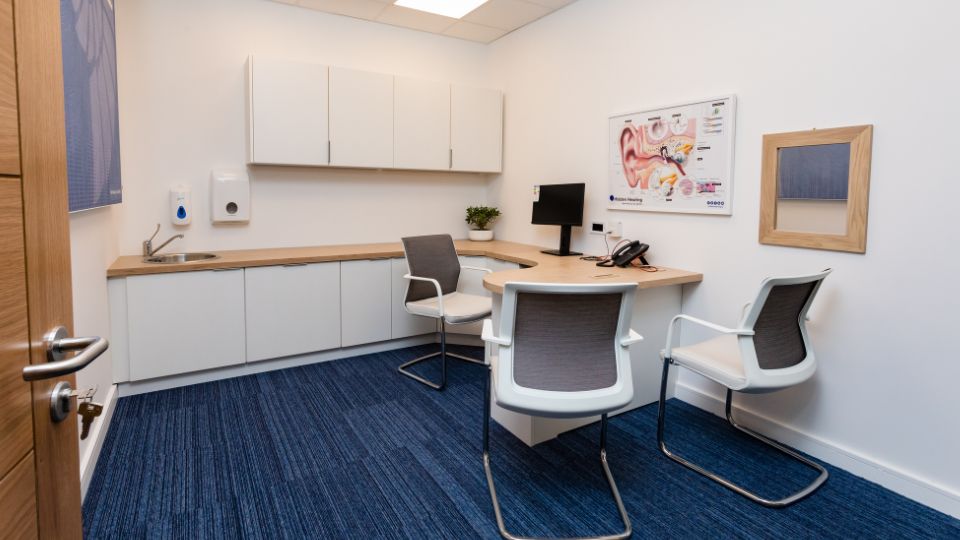 Interior of a Hidden Hearing clinic consultation room filled with audiological equipment and a graphic of a biological ear on the wall