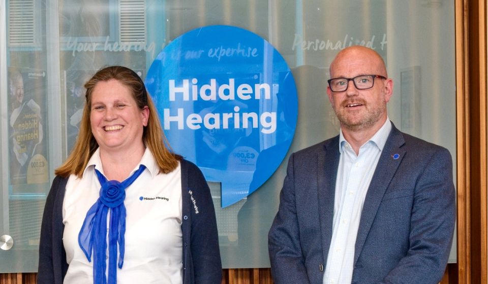 A picture of a Kilkenny clinic interior reception with audiologist Tom and clinic coordinator Aine standing in front of a Hidden Hearing logo