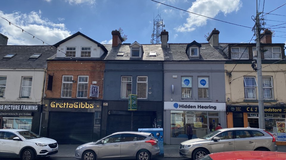 The image shows a Hidden Hearing clinic storefront with its signage, featuring a glass entrance. Parked cars line the street, and neighboring businesses include 'Gretta Gibbs' and shops with framed windows.