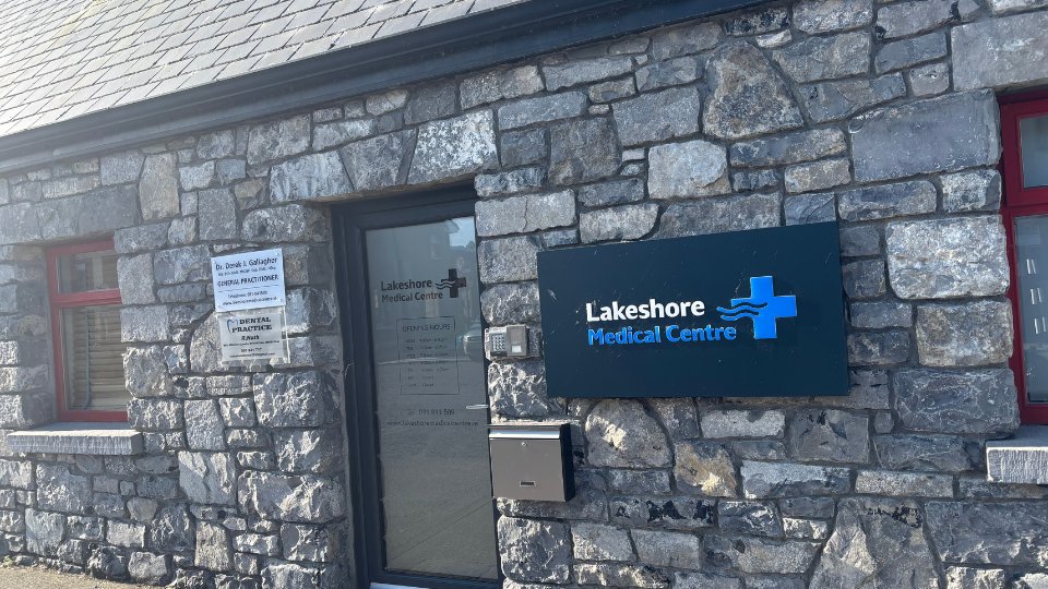 [GEN] A stone-built medical building features a sign for 'Lakeshore Medical Centre' with a blue cross logo. The entrance door lists opening hours and services, alongside a 'Dr. Derek J. Gallagher' general practitioner plaque.