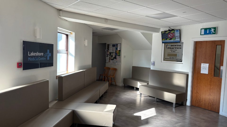 A waiting area with beige seating, a sign reading 'Lakeshore Medical Centre,' a window, bulletin boards, and a door labeled 'Dental Practice First Floor.' Emergency exit signage is visible.
