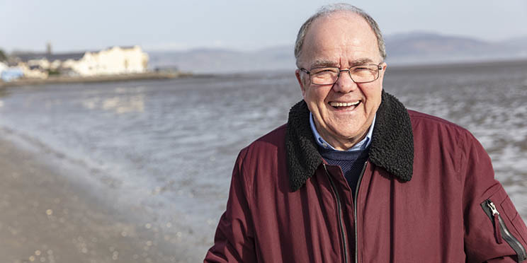 man walking along a beach in a burgundy jacket