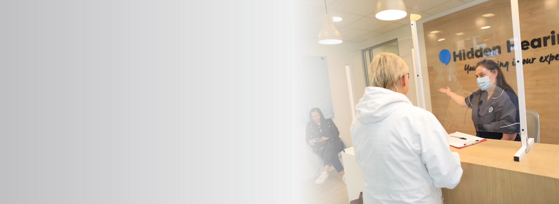 staff member at a hearing clinic gesturing to assist a customer