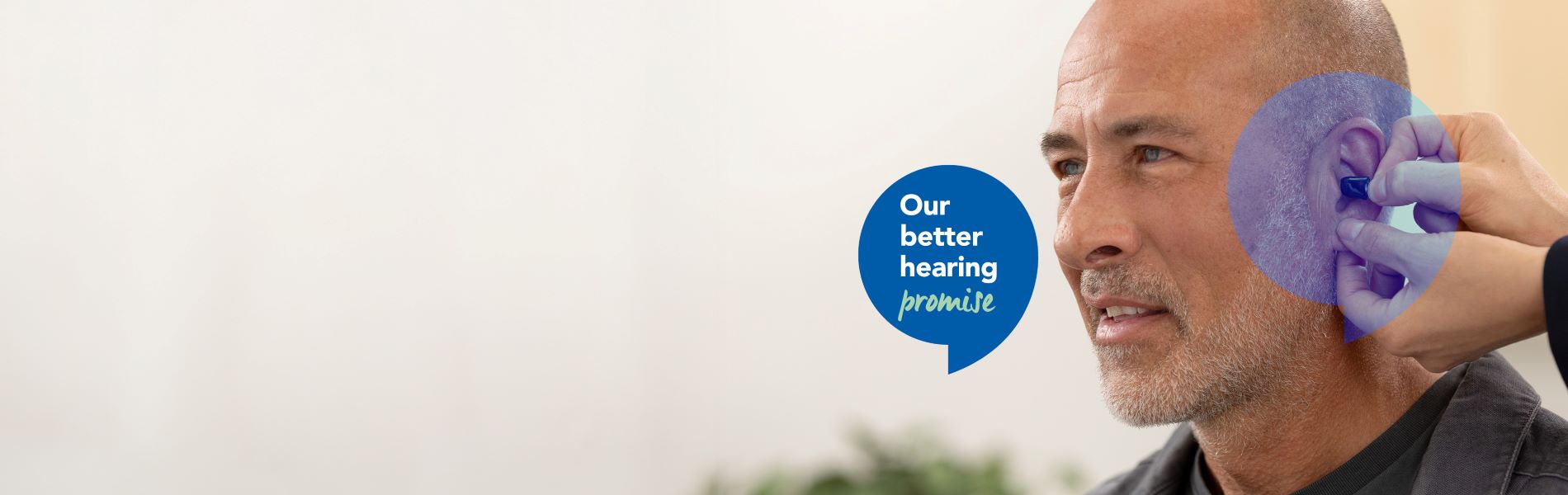A man getting a hearing aid inserted into his ear with a blue speech bubble highlighting our better hearing promise