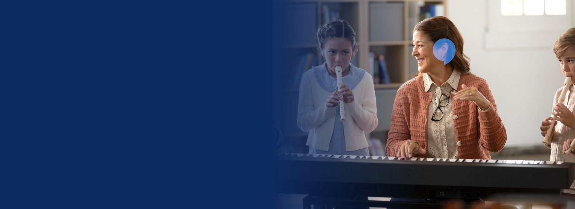 Teacher wearing hearing aids teaching music to children playing recorders.