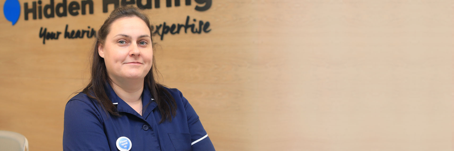 Hearing care professional wearing a navy uniform standing in front of Hidden Hearing signage.