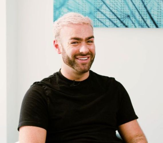 Man in a black t-shirt with short blonde hair and a beard smiling