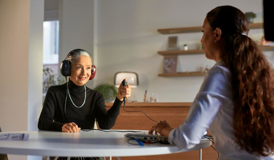 Image shows audiologist placing hearing aid on woman with hearing loss
