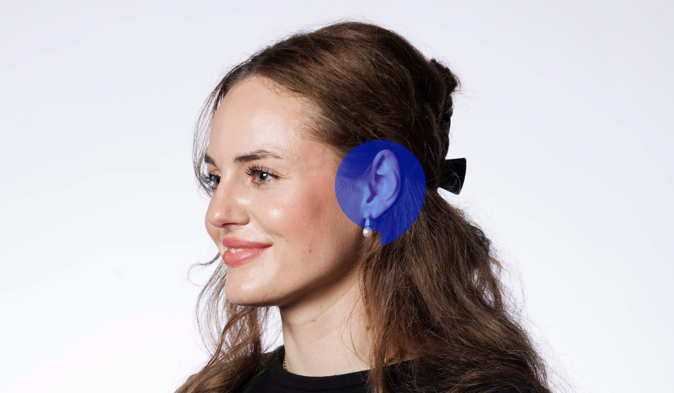 Audiologist fitting a hearing aid behind a woman's ear.