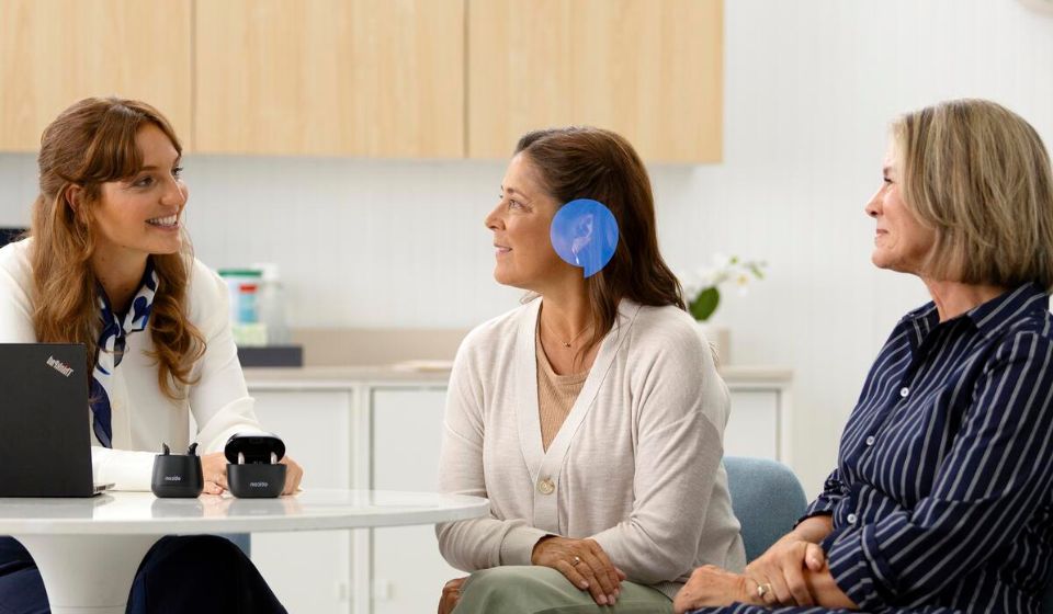 Woman consulting with a hearing care specialist during a hearing test, with hearing devices visible on the table.