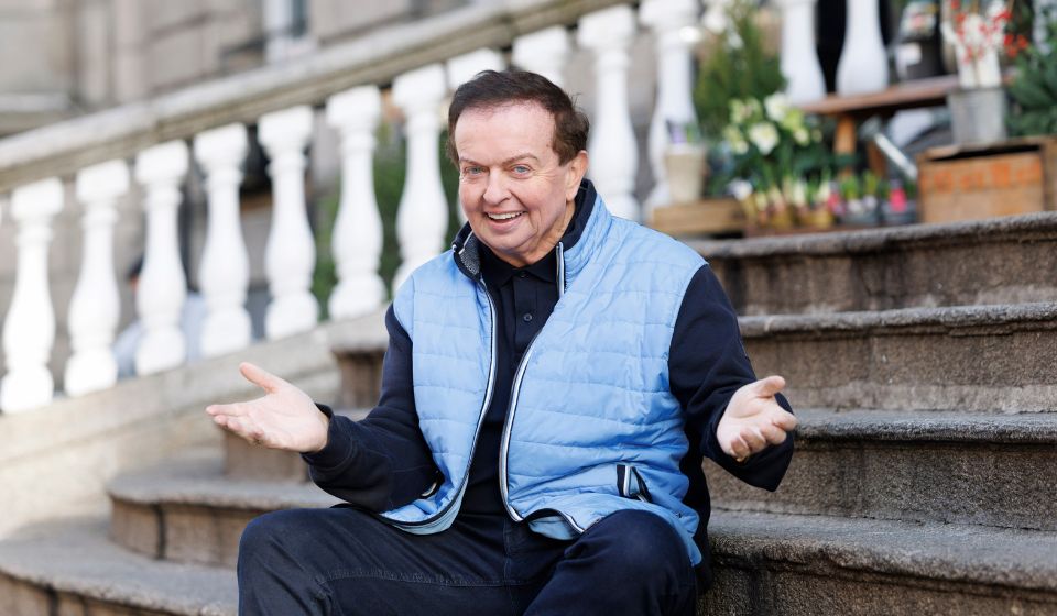 Presenter Marty Morrissey sitting with his hands out while smiling and sitting on stone steps