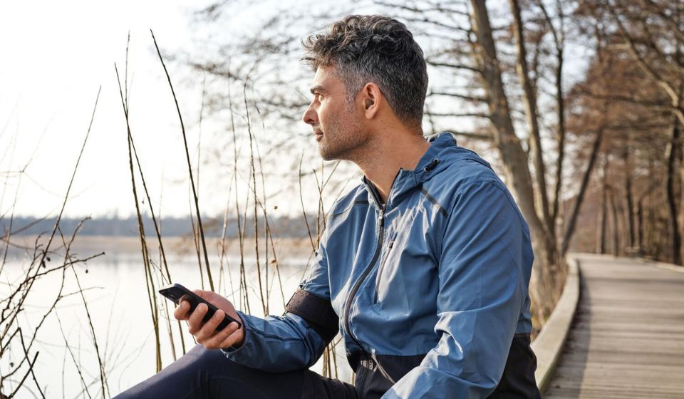 Man in a blue jacket on his phone while sitting and looking out at a lake