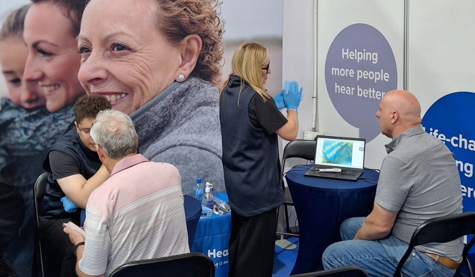 Individuals getting their ear examined with a video otoscope by a Hidden Hearing hearing care professional