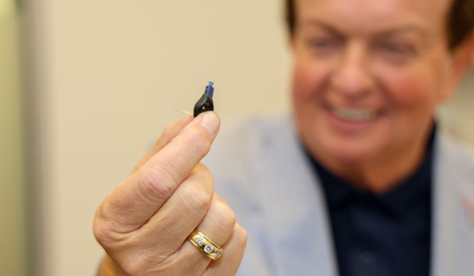 Marty Morrissey holding a small discreet hearing aid Oticon Zeal