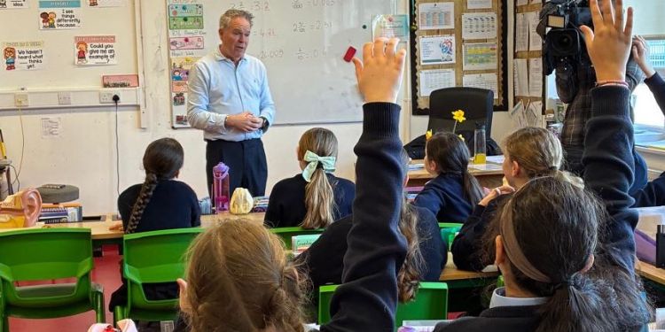 A picture of a classroom who are getting an educational talk about hearing health with two girls having their hands up to ask a question